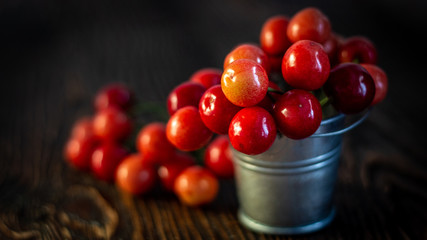 Fresh red Cherries in small metal bucket on old wooden background rural style