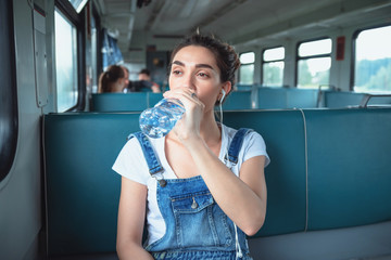 Young woman traveling by train. She drinking water from a plastic bottle while looking out the window