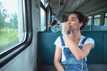 Young woman traveling by train. She drinking water from a plastic bottle while looking out the window
