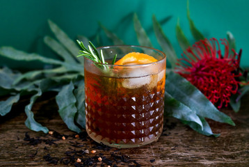 Old fashioned rum or whisky cocktail in front of a botanical, tropical dark green background.	