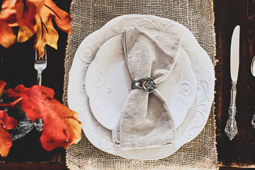 Thanksgiving Day or autumn place setting with napkins and cutlery on burlap table runner over a...