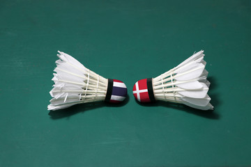 Two used shuttlecocks on green floor of Badminton court with both head each other. One head painted with Thai flag and one head painted with the Denmark flag.