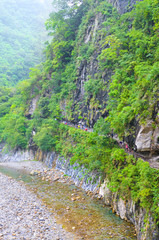 Fototapeta na wymiar Vertical photo of Taroko National Park in Taiwan. Named after Taroko Gorge by the Liwu River. Green tropical forests surrounded by steep rocks. Taiwanese landscape. Tourists hiking on path