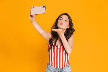 Portrait of lovely caucasian woman in striped t-shirt taking selfie on smartphone and sending air kiss