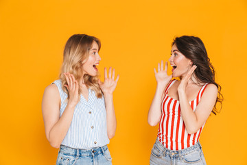 Portrait of two lovely blonde and brunette women 20s in summer wear expressing delight while raising arms