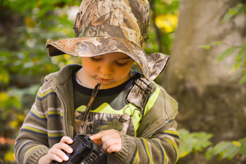 A small child in the forest at a picnic is considering a column to the smartphone for music