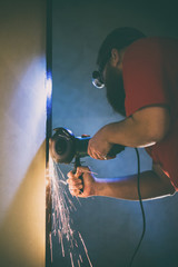 A man repairs a door in the basement of his house using a manual grinding machine.