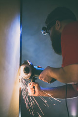 A man repairs a door in the basement of his house using a manual grinding machine.