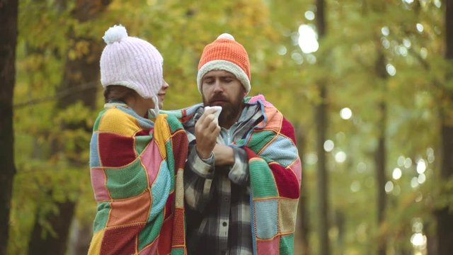 Sick people has runny nose. Woman makes a cure for the common cold in autumn park. Man with allergy symptoms blowing nose.