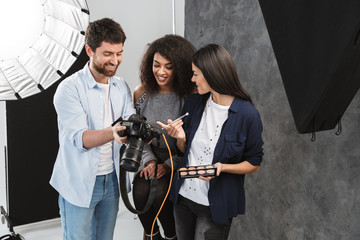 Fototapeta na wymiar Portrait of happy multiethnic people looking at professional camera while photographer shooting female model in studio