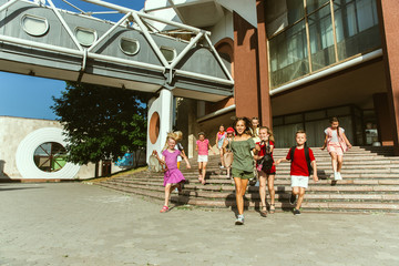 Happy kids playing at city's street in sunny summer's day in front of modern building. Group of happy childrens or teenagers having fun together. Concept of friendship, childhood, summer, holidays.
