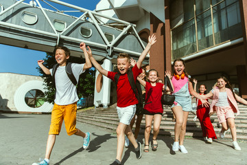 Obraz premium Happy kids playing at city's street in sunny summer's day in front of modern building. Group of happy childrens or teenagers having fun together. Concept of friendship, childhood, summer, holidays.