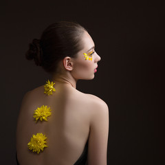 Young woman spa. Yellow flowers along her back, face and body in the shade. Back view. Dark background