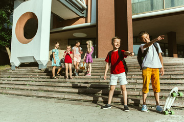 Happy kids playing at city's street in sunny summer's day in front of modern building. Group of happy childrens or teenagers having fun together. Concept of friendship, childhood, summer, holidays.