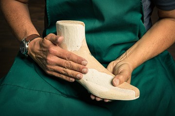 close up of orthopedic shoemaker hands checking quality of a wooden last