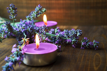 Spa massage setting with lavender flowers, scented aroma candles on wooden background. Close-up. Copy space.