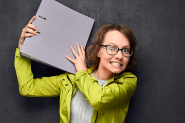 Portrait of angry girl trying to hit someone with folder
