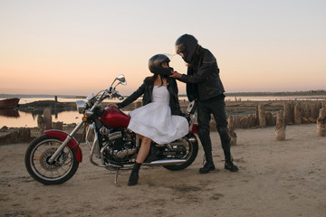 Fototapeta na wymiar Romantic biker couple in leather and helms with red motorcycle. Woman and man against motorcycle and sunset, sunrise