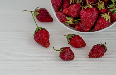 Fresh summer ripe strawberries in a white plate on a white wooden background