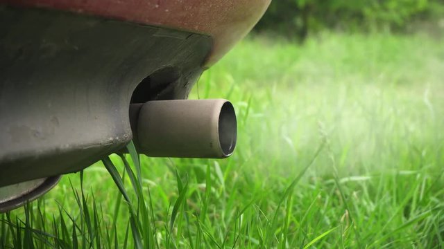 Machine pipe smoke condensate water. Closeup of machine exhaust pipe releasing fumes in the air. Green grass