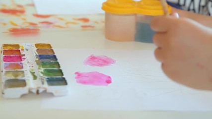 The children's hand of the artist picks up paint on the brush. The child is passionately engaged in creativity. The child draws gouache on paper. Developing lesson.
