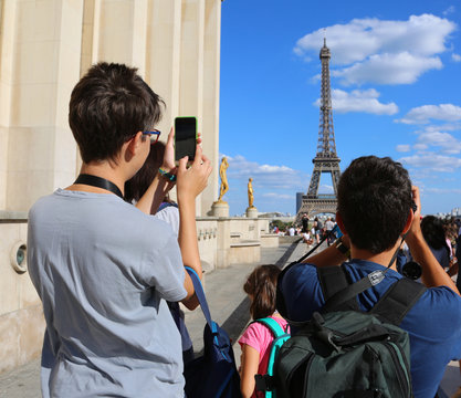 Young tourists take pictures of Eiffel Tower in Paris France fro