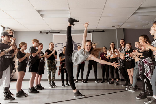 Dancers cheering young woman screaming while standing on one leg in dance studio