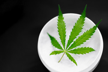 Top view of a jar with CBD or hemp salve with cannabis leaf on black background. Marijuana cream....