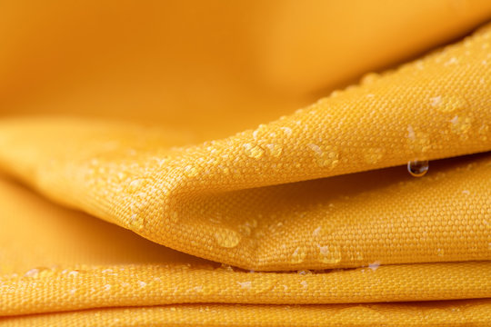 Close-up waterproof and water repellent fabric.  Water drops on textile. Folded canvas of yellow fabric