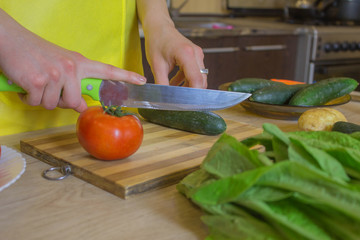 Chef cuts the vegetables into a meal. A woman uses a knife and cooks. Woman's hands cutting vegetables, behind fresh vegetables