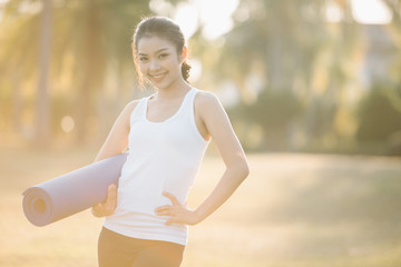 Fototapeta premium woman carrying a yoga mat outdoors and smiling