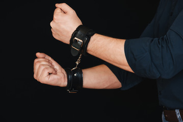 man's hands in leather handcuffs on black background