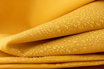 Close-up waterproof and water repellent fabric.  Water drops on textile. Folded canvas of yellow...