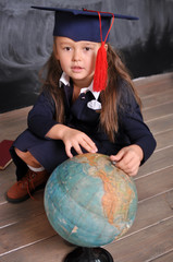 Fototapeta premium Portrait of happy school girl in graduation hat.Go to school for the first time.Young first-grade girl exploring the globe.school and education concept