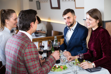 Group of cheerful friends enjoying evening meal at restaurant