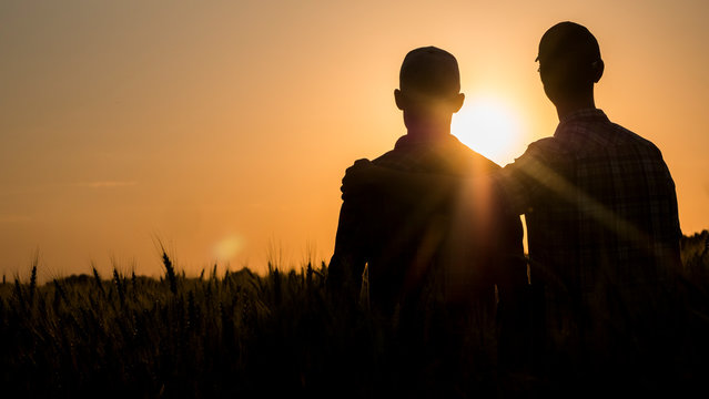 Two men gently hugging at sunset, rear view