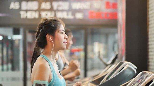 Young beautiful woman asian with friend running on a treadmill at gym. Fitness and healthy lifestyle concept. Slow motion