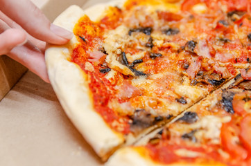 Female hand takes a piece of pizza from the box on the kitchen table close up