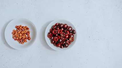 Halves of berries dark red cherries and separated bones in different white bowls on white background