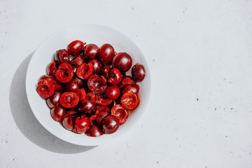 Cut halves of ripe berries dark red cherries in white bowl on white background