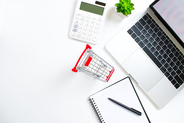 Top view which consists of a laptop, computer, shopping cart, pen book and calculator on a modern style desk. Online shopping concept