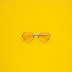 Yellow transparent sunglasses lie on a center of bright yellow background.