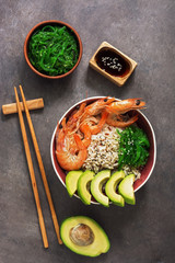 A bowl of sushi shrimp, rice, avocado, seaweed chuka, soy sauce and chopsticks on a dark background. Asian food. Top view, copy space.