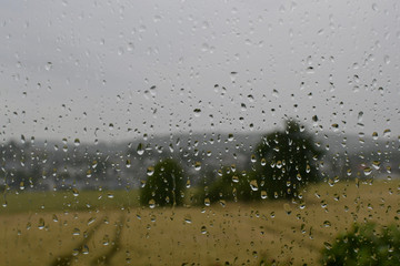 bad weather rainy day depressive mood raindrops on window pane with blurred background agricultre wheat field