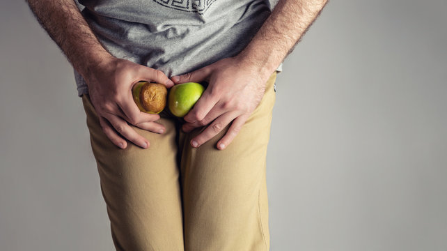 A man in beige jeans clenched his legs and at the level of the genitals, holding a ripe and rotten Apple. Disease for men. The concept of protection against sexually transmitted infections.