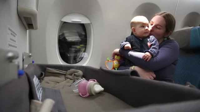  Mother with a very impressed of first flight small child on the plane, a woman holds the infant baby in her arms, hugs and kisses her.