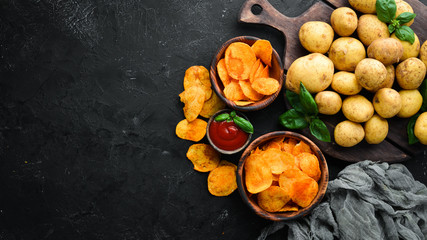Potatoes and potato chips on a black background. Organic food. Top view. Free space for text.