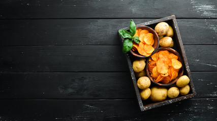 Potatoes and potato chips on a black background. Organic food. Top view. Free space for text.