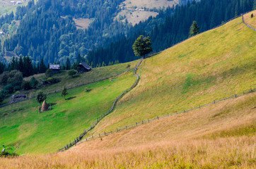 Fototapeta premium An old farmer's wooden house stands on an elephant mountain near a haystack against the backdrop of mountain peaks