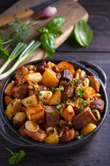 Fried beef and  potatoes with onions and garlic served in black dish on wooden background